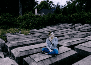 Person sitting on a grave stone, smoking a cigarette